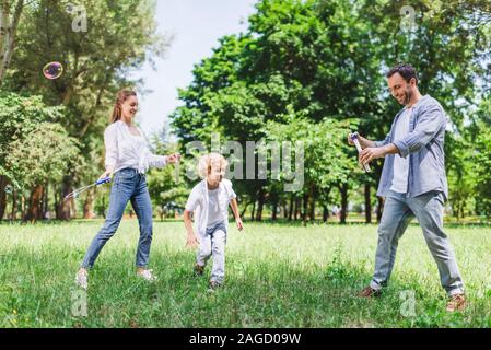 mother, father and son playing with soap bubbles in park Stock Photo