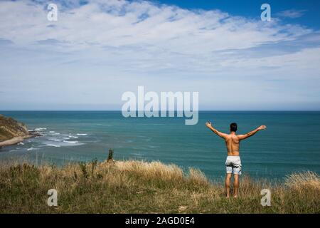 Athletic male standing on a hill near the sea with stretched hands feeling free of everything Stock Photo
