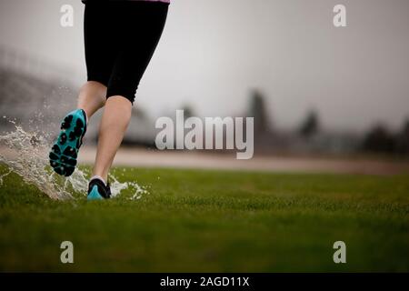 Young woman jogging on a sports field in the rain. Stock Photo