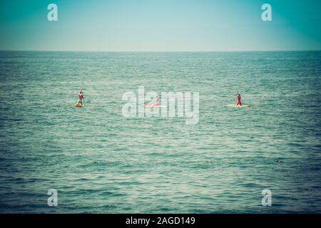 A rear view of Two bikini clad women and a man kneeling as they maneuver their stand up paddle boards out toward the Pacific Ocean from  Santa Barbara Stock Photo