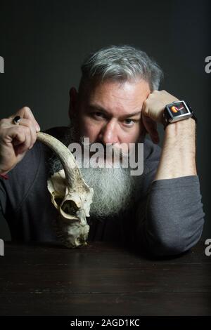 Dark portrait of a bearded middle-aged man with an animal skull, selective focus Stock Photo