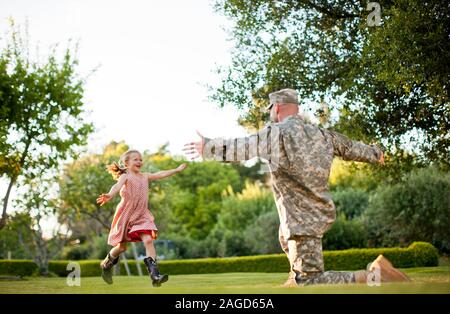 Young girl running towards her father with her arms out in their back yard. Stock Photo