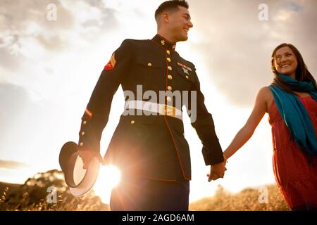 Smiling military soldier holding hands and smiling at his girlfriend while walking in the sunshine. Stock Photo