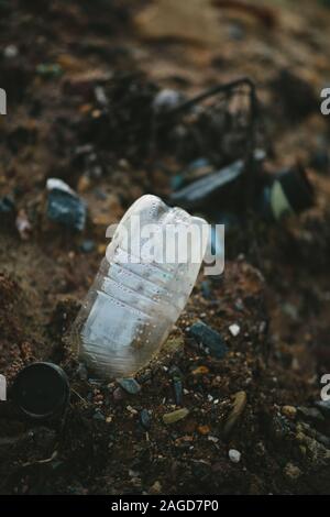 Closeup of a plastic bottle in a ground surrounded by garbage with a blurry background Stock Photo