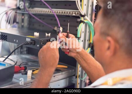 Rack Mounted Servers In A Server Room, man work with lan or network cables. Stock Photo