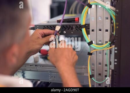Rack Mounted Servers In A Server Room, man work with lan or network cables. Stock Photo