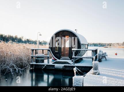 wooden sauna hut covered in snow on a jetty on lake in Sweden Stock Photo