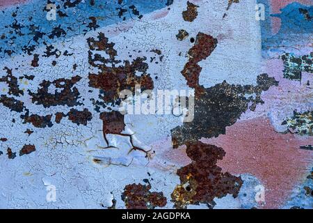 Surface of old rusty metal doors painted in various colors. The layers of azure, blue and red paint are bounced and cracked from the weather. Abstract Stock Photo