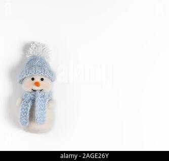 Cute funny snowman in blue hat and scarf on white background. Christmas wool toy. Copy space. Happy new year. Winter concept. Greeting card. Stock Photo