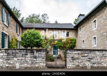 Breinig-Stolberg, Germany - Sept. 08, 2019: Traditional farm house built around a central compound, and iron entrance gate with rose bushes. Mansion b Stock Photo