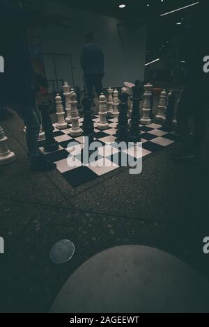 Vertical shot of a large floor chessboard with big figures and people playing Stock Photo