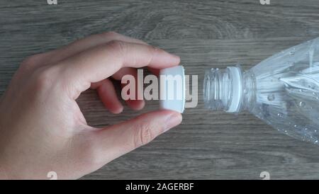 Closeup of the mouth of a clear plastic bottle, with a hand holding the white cap. Stock Photo