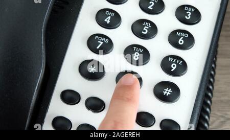 Hand pressing the 0 dial key of an office phone. Stock Photo