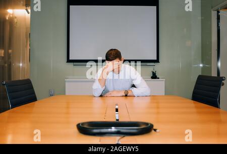 Man sat in a meeting room with his head in his hands looking stressed Stock Photo