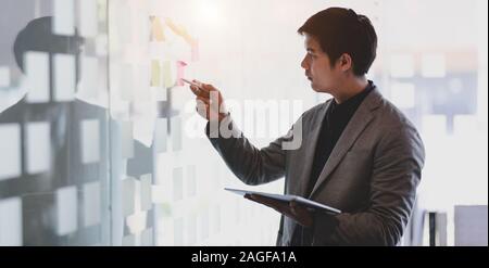 Young businessman working on his project while picking up the idea from sticky notes Stock Photo