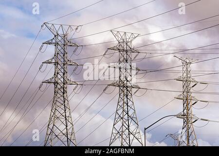 High voltage electricity power lines and transmission towers; sunset colored clouds visible in the background; California Stock Photo