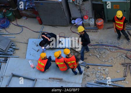 Bangkok, Thailand - December 16, 2019 : A worker at construction site kneeling and welding steel bars together, his coworkers are standing around Stock Photo