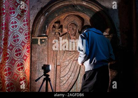 Eth1041Ethiopia, Amhara Region, Lalibela, Bet Golgotha, inner sanctum, conservator examining carved stone  life size apostle figure with bright light Stock Photo