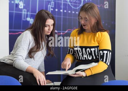 Campus life, students friendship.Two female students helping each other inside classroom. Education, dating, lifestyle concept. Stock Photo