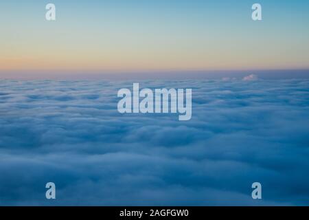 Endless aerial view above fluffy clouds at sunset from the top of a mountain in winter, a beautiful nature landscape Stock Photo