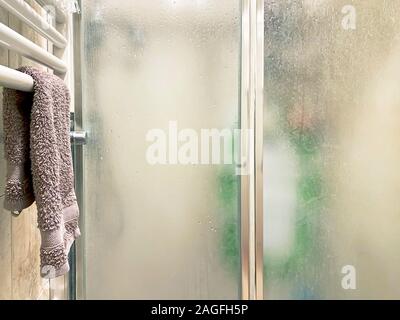 violet colored towel laid out on a white radiator near the shower enclosure with frosted glass doors and aluminum structure inside a bathroom. Interio Stock Photo
