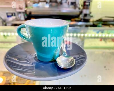 close up of a cup of turquoise coffee on a saucer and with the steel spoon served on the glass counter of an Italian bar. Take a break with a coffee a Stock Photo