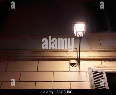 Antique decorated wrought-iron street lamp attached to the wall of an old building in the historic center of Rome at night. Glare of light on the wall Stock Photo