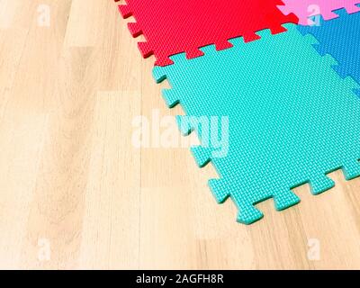 Soft rubber mat composed of colored blocks intersected with each other on a wooden floor. Suitable for children to play or for yoga exercises. Interio Stock Photo