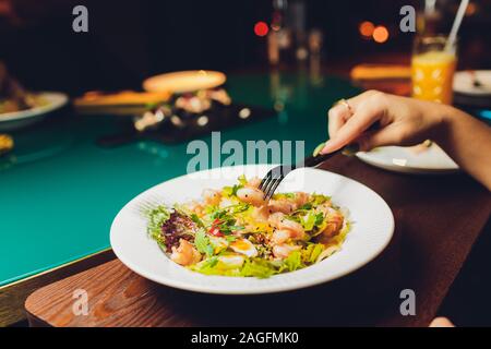 Restaurant or cafe table with plate of salads and wine. Two people talking on background. Toned picture Stock Photo
