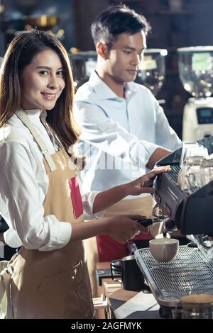 Side view shot of a female barista making a cup of coffee with other barista working in background Stock Photo