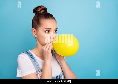 Turned photo of shocked person inflating baloon looking wearing white t-shirt denim jeans overall isolated over blue background Stock Photo