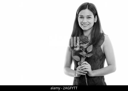 Studio shot of happy young beautiful woman smiling and holding red rose ready for Valentine's day Stock Photo