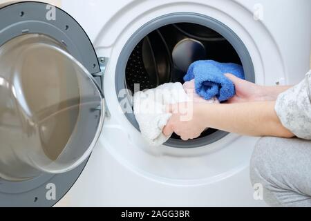 woman loading dirty towels into modern washing machine in white case with open door close view Stock Photo