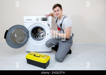 professional master with wrench and toolbox near modern washing machine on wooden floor near beige wall looking at camera Stock Photo