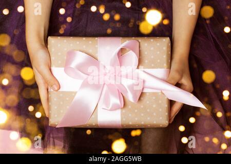 Luxurious gift in girl's hands on the purple background. Perfect bow. Concept of the New Year, Christmas, Valentine's Day, gifts Stock Photo