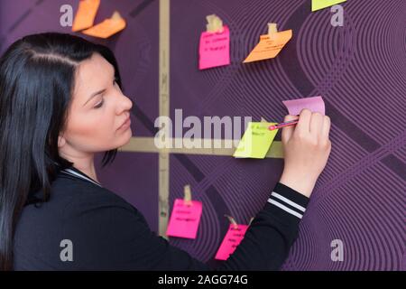 Young female employee in stylish spectacles using stickers for creation strategy of working project during brainstorming session, skilled team member Stock Photo