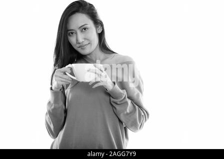 Studio shot of young beautiful Asian woman holding coffee cup Stock Photo