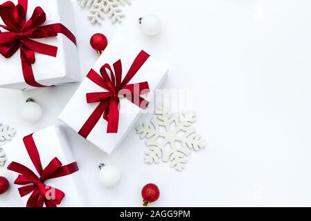 Border from gift boxes wrapped white paper and red ribbon decorated bubles and snowflakes on white background. Top view. Flat lay.  Christmas and