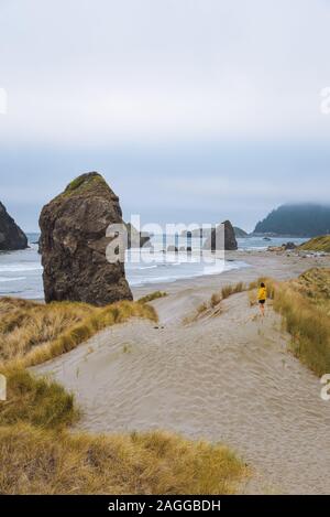 Lone female hiker on rugged coastal beach on moody afternoon, Oregon, USA