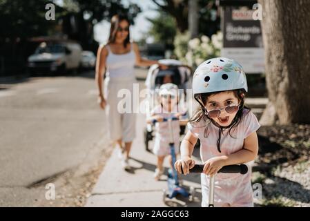 Mother and daughters playing push scooter in neighbourhood Stock Photo