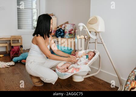 Mother comforting crying baby girl in bouncer Stock Photo