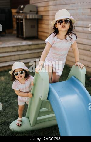 Sisters playing on slide in backyard Stock Photo
