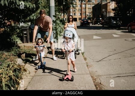 Couple and daughters playing push scooter in neighbourhood Stock Photo