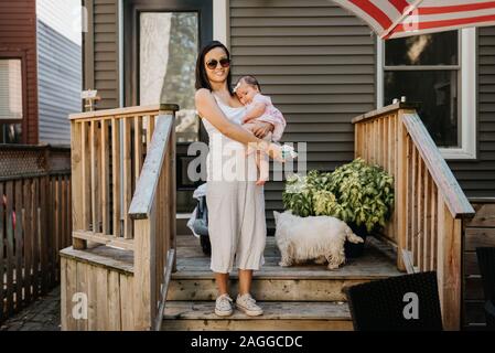 Mother with baby girl in arms accompanied by pet dog on stairway Stock Photo