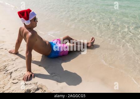 Young handsome man in santa hat from the back on beach of ocean Stock Photo