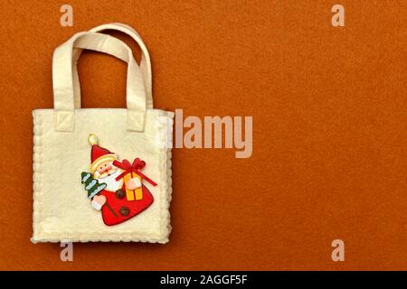 Handbag with handles, with decorative wooden figurine of Santa Claus sewn in the corner, on a red felt background. Stock Photo