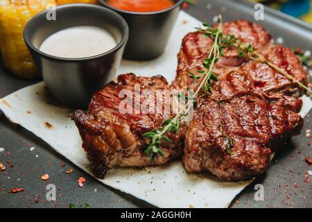 A juicy grilled meat steak with two sauces sits on a black square plate . Hot Meat Dishes. Stock Photo