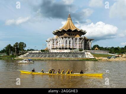 Longboat passing by the Sarawak State Legislative Assembly Building, by the Sarawak river, Kuching, Sarawak, Borneo, Malaysia Stock Photo