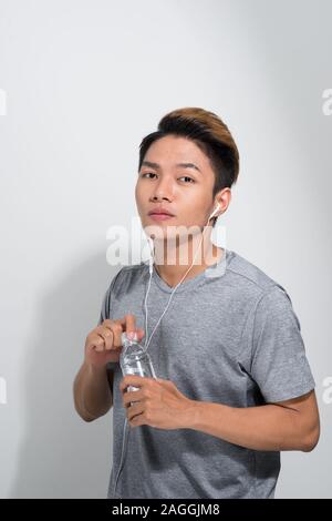 Young sports Asian man wearing earphones and holding water bottle on white background. Stock Photo