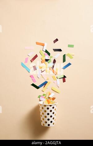 Drinking paper cup with multicolored confetti scattered on party background. Greeting card poster template. Copy space Stock Photo